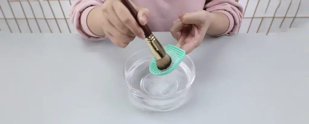 Pouring cleanser onto a cleaning pad for how to clean makeup brushes step by step.