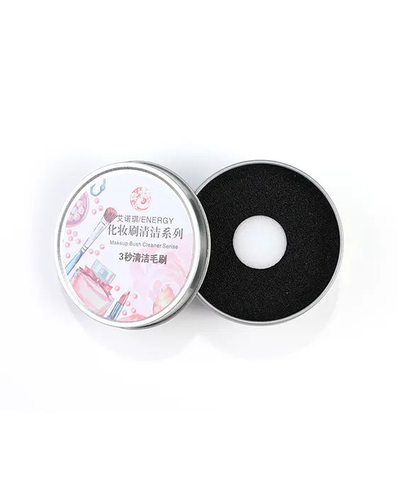 Open view of the black circular dry cleaning sponge revealed inside its metal case, with pink-handled makeup brush nearby, demonstrating the sponge's textured surface for quick powder absorption.