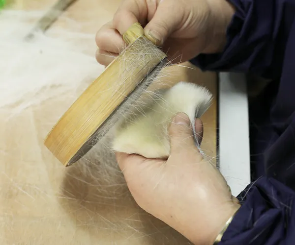 Worker pre‑combing makeup brush fibers on a board to loosen and clean the bristles before selection.