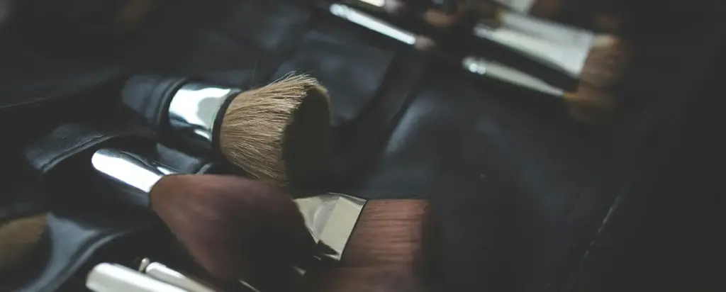 A set of professional makeup brushes laid out on a black leather mat, showing different makeup brushes types and their uses.