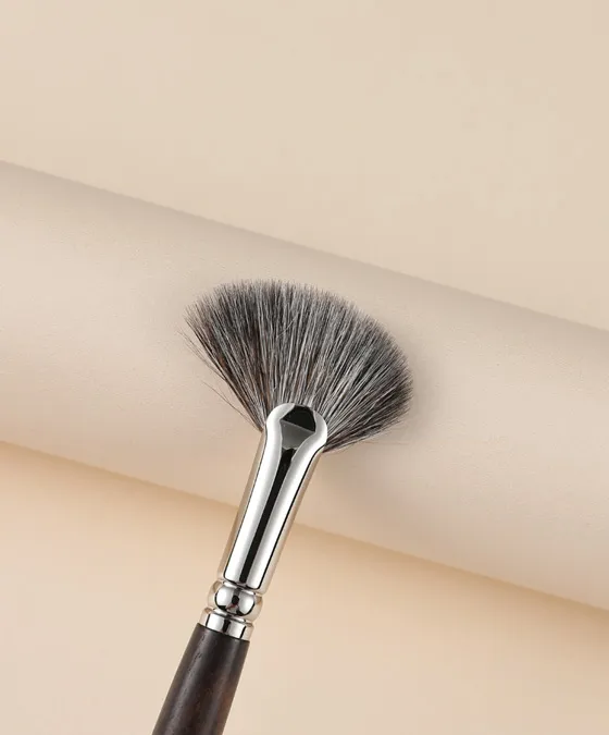 Ainochi S6412 angled fan highlighter brush side angle with handle on cream surface, professional blue squirrel fan highlighter brush for seamless glow